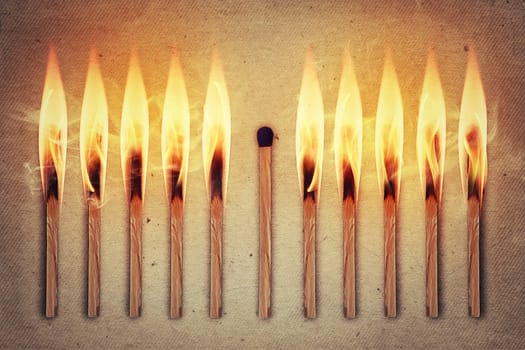 Whole, unused match standing middle a row of burning matches. Standing out from the crowd, leadership concept