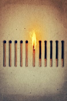 Burning match standing middle a row of whole, new matches at left and extinguished at right. Leadership concept