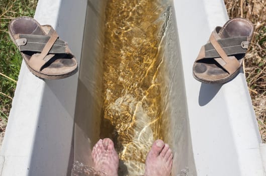 Man feet refreshing in a cool irrigation canal during the hottest day hours, Vegas Altas del Guadiana, Spain