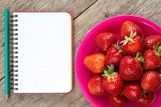 Pink plate with strawberries and blank notebook with pencil