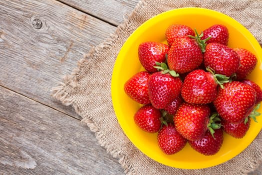 Yellow plate with strawberries on piece of sackcloth