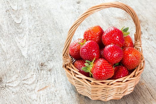 Red strawberries in wicker basket on a wooden background