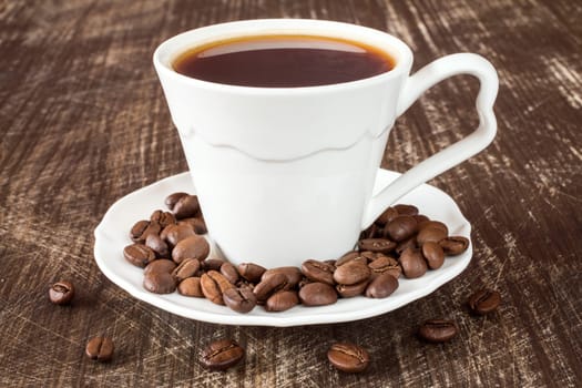 White coffee cup with roasted coffee beans on wooden background.