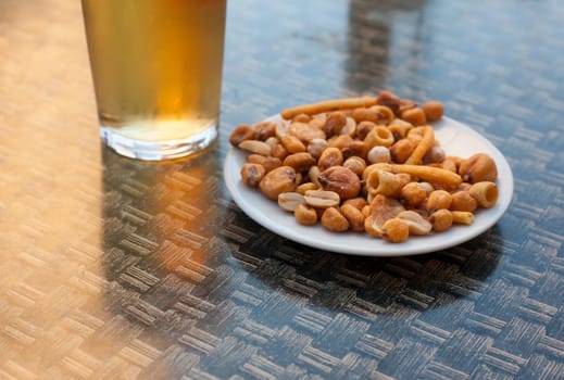 Cold glass of beer over terrace table with snack of dried fruit and nuts