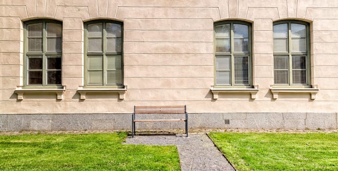 Bench in front of Windows on building with grass.
