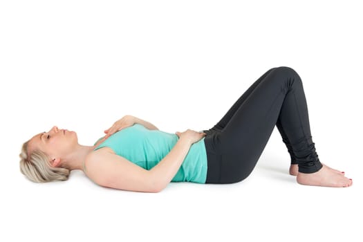 Full body view of a young blonde woman doing yoga exercises against a white background with a slight shadow
