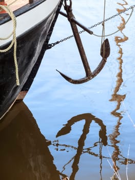 Bow of a cutter with overhanging anchor and water reflection