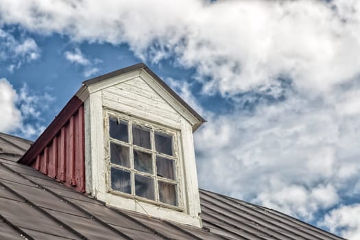 Weathered Window on Roof with a cloudy sky.