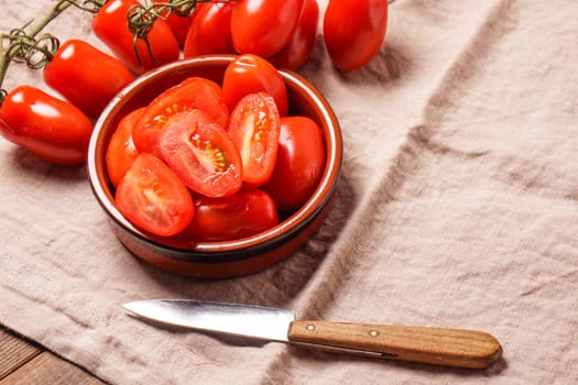 Ripe Organic red plum tomatoes. There is some whole tomatoes and other cut in a bowl