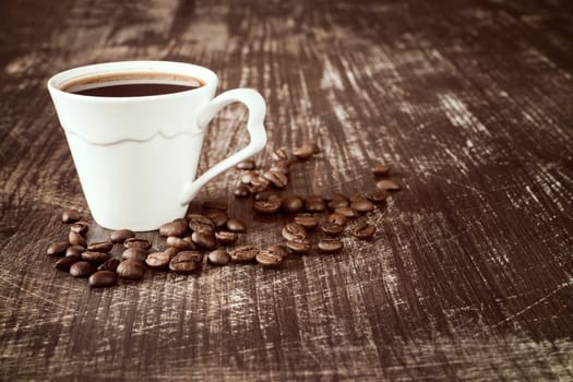 Coffee cup with roasted coffee beans on wooden background.