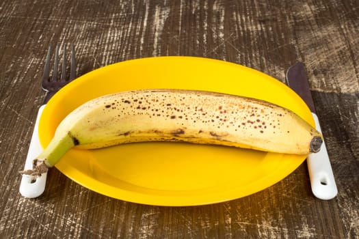 Fork,knife and plate with banana on wooden background.