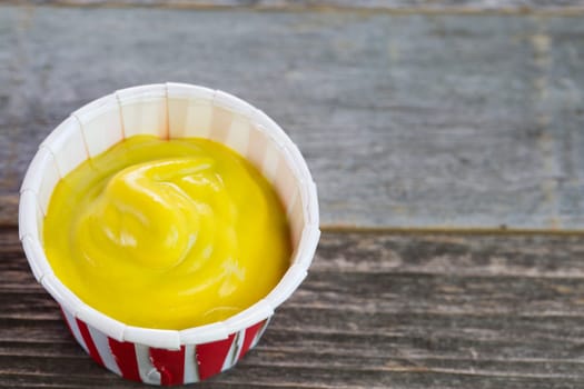 Mustard in a paper serving cup close up.