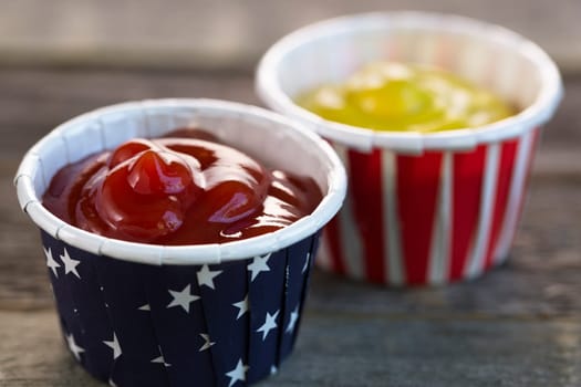 Ketchup and mustard in red white and blue paper cups ready for your BBQ