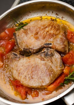 Pork chop with herbs and tomatoes in a steel pan