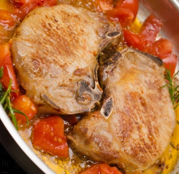 Pork chops with herbs and tomatoes in a steel pan
