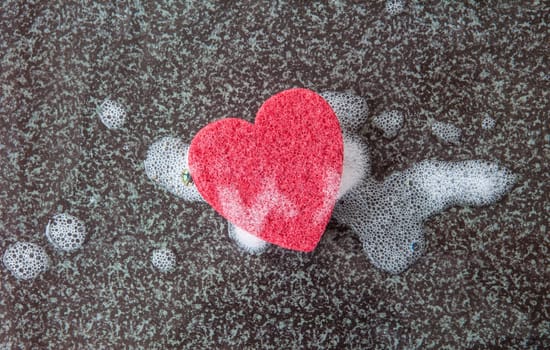 Red sponge in heart shape with detergent on a dark background