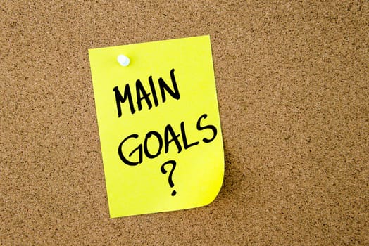 Main Goals ? written on yellow paper note pinned on cork board with white thumbtacks, copy space available