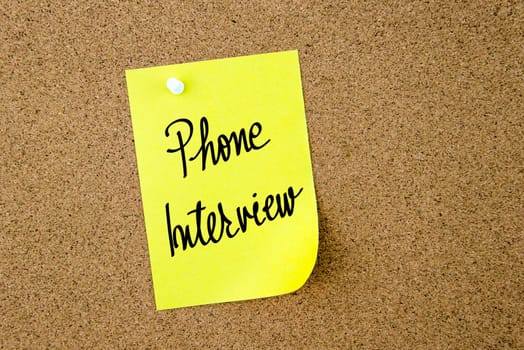 Phone Interview written on yellow paper note pinned on cork board with white thumbtacks, copy space available