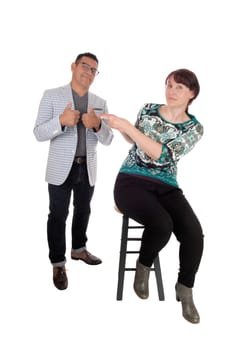 A unhappy middle age woman sitting on a chair pointing her finger at her.husband, he is smiling, isolated for white background..