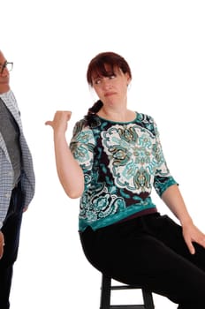 An upset woman sitting on a chair pointing back at her standing husband.looking unhappy, isolated for white background..