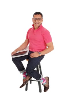 A happy Hispanic man sitting on a chair, smiling, with the mew's paper .and his tablet on his lap, isolated for white background..