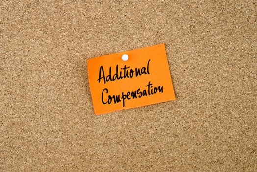 Additional Compensation written on orange paper note note pinned on cork board with white thumbtack, copy space available