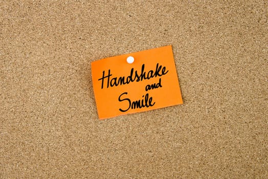 Handshake and Smile written on orange paper note note pinned on cork board with white thumbtack, copy space available