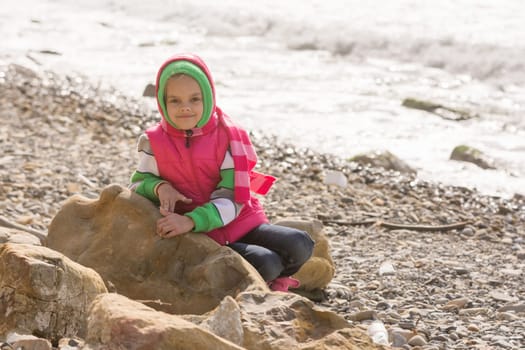 Happy girl sitting on a rock on the sea coast and looking at the frame