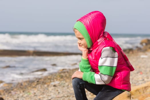 Girl sitting on the rocky beach and the sea head on his hand looking to the frame