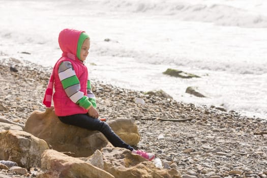 Happy girl sitting on a rock on the sea coast and looking into the distance
