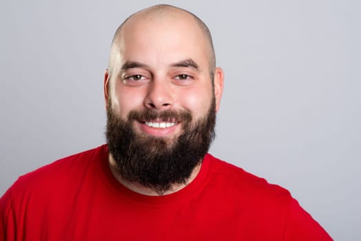young bearded man in red shirt in front of gray background