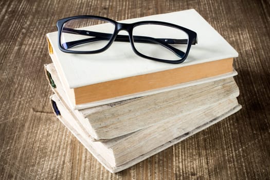 Books and reading glasses on the wooden background.