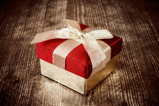Gift box with golden ribbon on the dark wooden floor