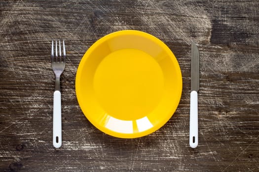 Empty yellow plate, fork and knife on wooden background. Top view with text space