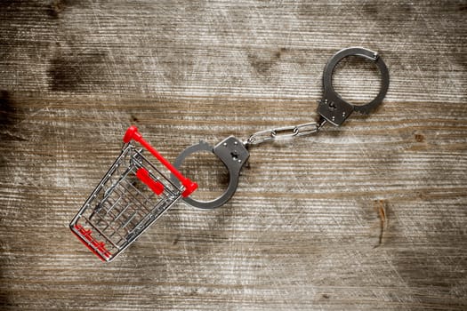 Shopping cart and handcuffs on old wooden background.Top view.