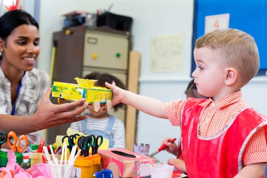Little boy in nursery showing his teacher the cereal box car he has made.