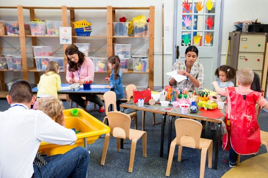 Class of nursery children doing arts and crafts with their teachers. They are using recycled boxes and cartons.