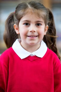 Portrait of a school girl. She is wearing a red jumper and smiling at the camera.