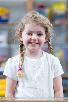 Portrait of a school girl. She is wearing a white top and smiling at the camera.