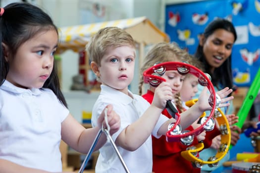 Nursery children playing with musical instruments in the classroom. One little boy is looking at the camera with a tambourine.