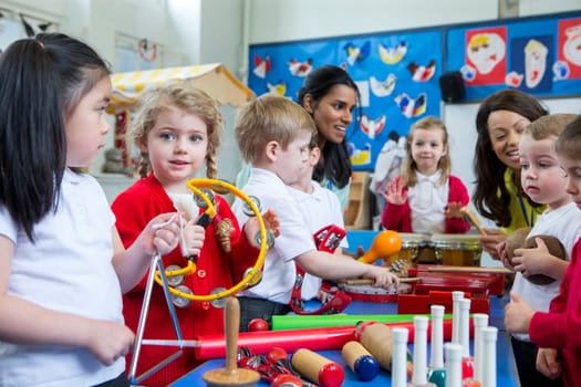 Nursery children playing with musical instruments in the classroom. One little girl is looking at the camera with a tambourine.