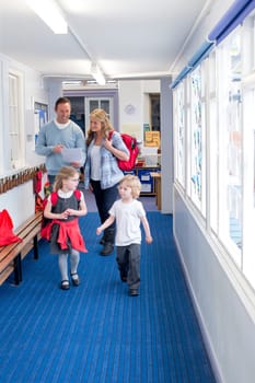 Parents and students walking down a primary school corridor. the parents are looking at some paperwork and the children are talking.