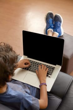 Latino boy sitting on sofa with laptop computer.