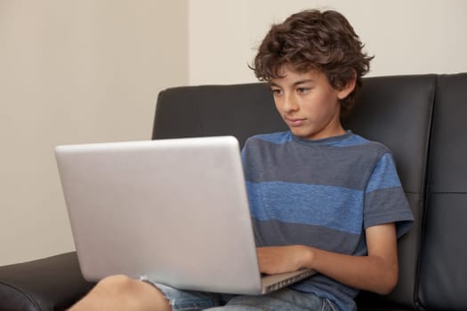 Latino boy sitting on sofa with laptop computer.