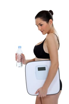 Young woman in underwear holding bottle of water and scales