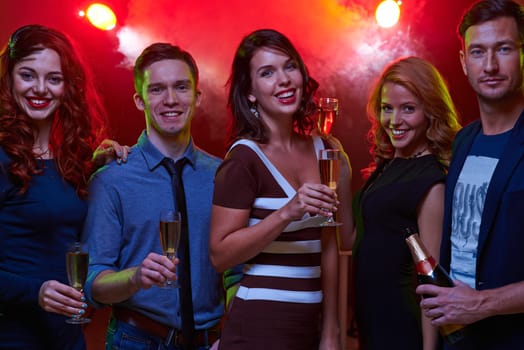 Group of friendly guys and girls with champagne enjoying party in night club