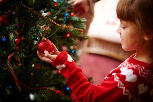 Cute little girl looking at red decorative toy bubble on xmas tree