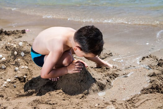 little boy in blue sea playing with mud pies and sand
