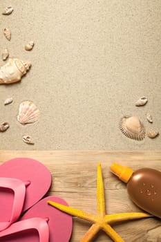 summer concept with pink flip flops,yellow starfish,suntan oil and shells on sandy beach background. top view