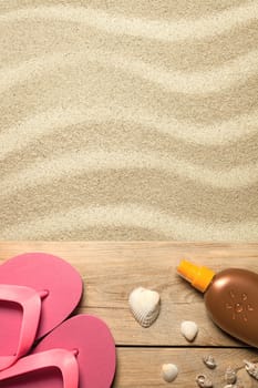 summer concept with pink flip flops,shells and suntan oil on sandy beach